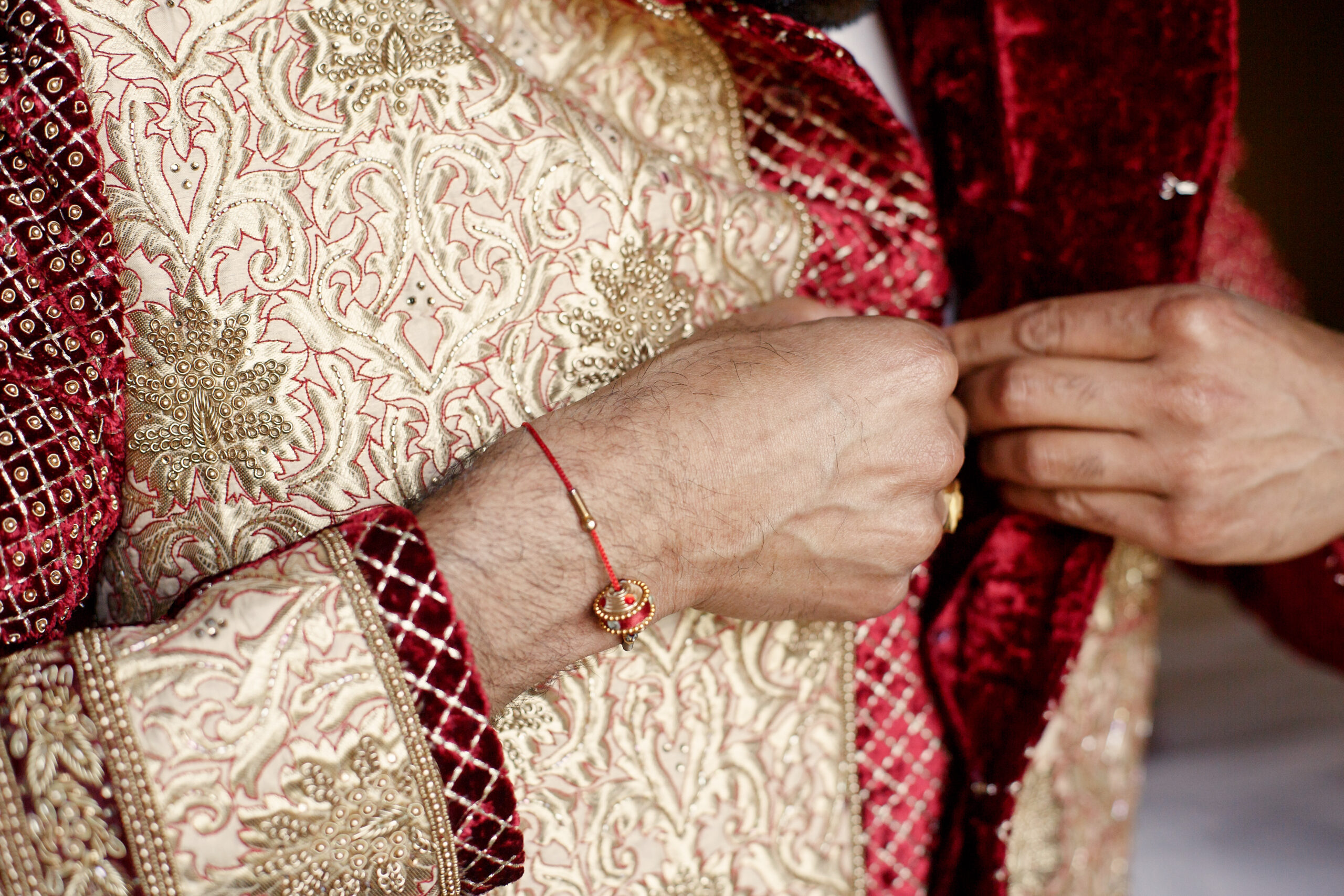 Groom's arms with red bracelet button up golden wedding suit